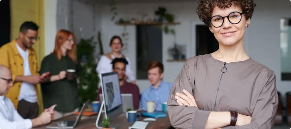 Professional woman with glasses smiling with arms crossed in a modern office
